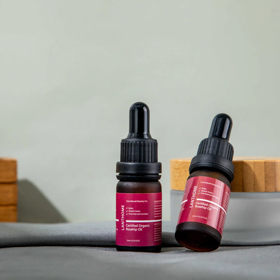 Close-up of Lanthome Certified Organic Rosehip Oil dropper held above an amber bottle, with focus on the clear serum and blurred skincare elements in the background, featured on Rosvia.